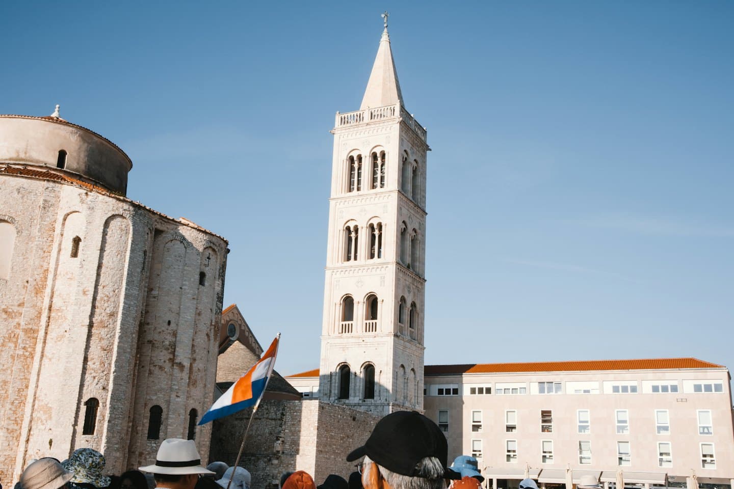 Persone riunite all'aperto che guardano una storica chiesa in pietra in una giornata di sole.