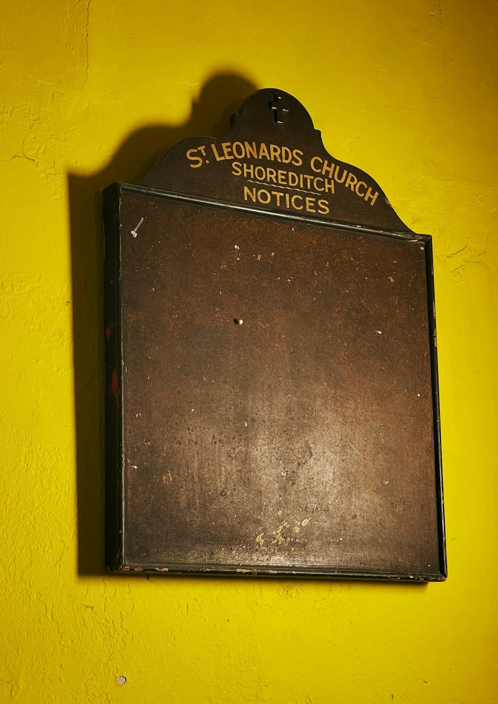 Bacheca in legno della chiesa di San Leonardo su un muro giallo.