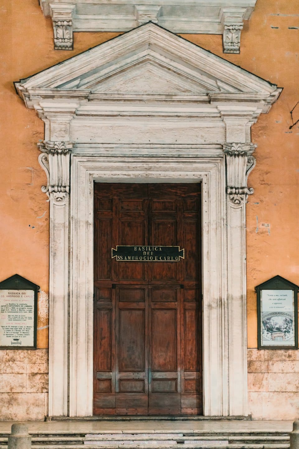 Ingresso di una chiesa in pietra ornata con porte di legno e bacheche informative.